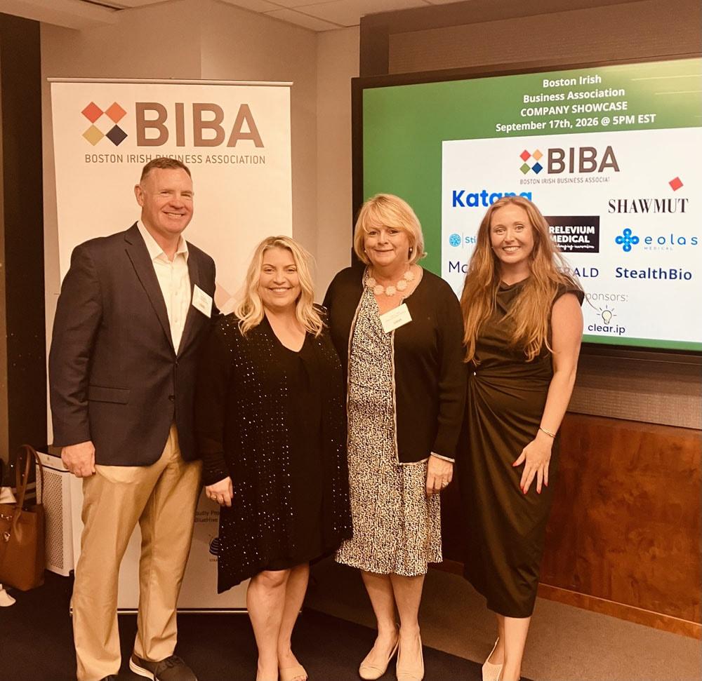Four attendees at the BIBA Company Showcase, standing between a BIBA banner and a screen listing the showcase companies